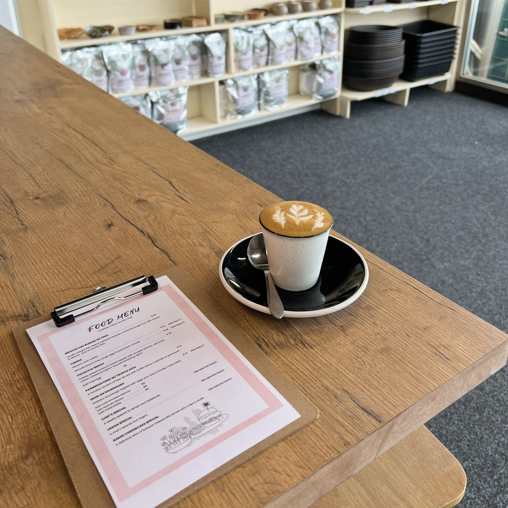 Showcasing the Kusamono Café food menu and a cup of coffe sitting beside each other on a wooden table.