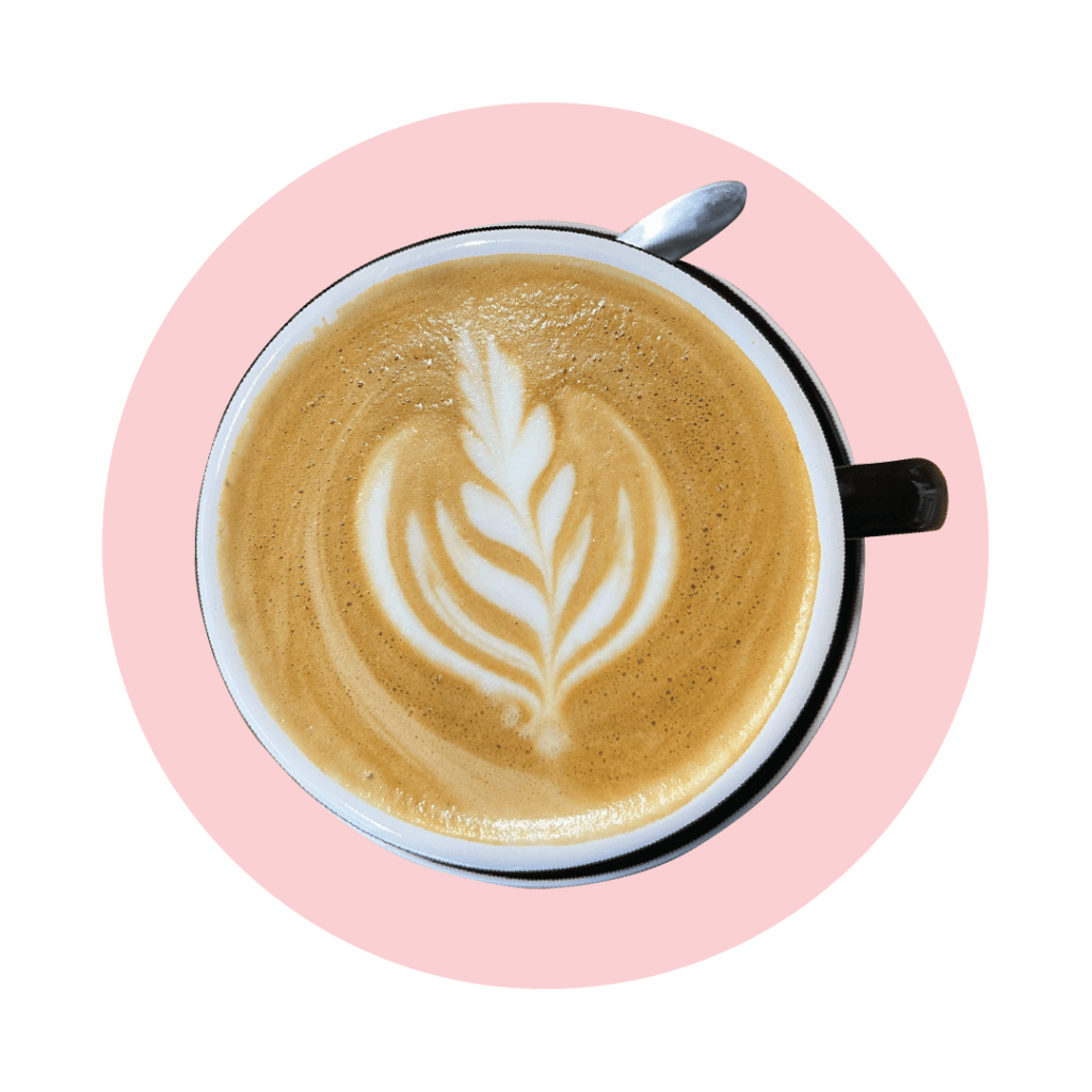 A Kusamono coffee in a black mug set with coffee art of a fern, contained in a pink circle.